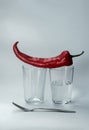 A glass cup half full of water stands on a light background. Red pepper lies on a glass. Close-up