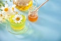 Glass cup of healthy herbal camomille tea with camomille flowers and jar of honey on the blue background. Naturopathy. Matricaria