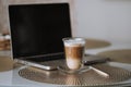 A glass cup with a double bottom with a fragrant hot latte cappuccino stands on the table morning breakfast computer laptop and wo Royalty Free Stock Photo