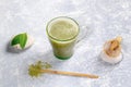 Glass cup with matcha green tea, wooden spoon with powder, bamboo whisk and leaves on stones on grey textured backdrop. Royalty Free Stock Photo