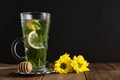 Glass Cup of mint tea ith lemon slices and yellow flowers on background. Wooden table and black background. Royalty Free Stock Photo