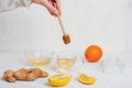 Glass cup with orange, lemon and ginger tea and honey pouring into a cup. Ingredients on white wooden table Royalty Free Stock Photo