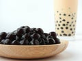 A glass cup of pearl milk tea also called bubble tea and a plate of tapioca ball on white background.