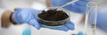 Glass cup with soil sample stands on hand in rubber glove in chemical laboratory closeup