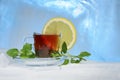 Glass cup of strong black tea on a beautiful blue ice with yellow lemon and green mint. Royalty Free Stock Photo