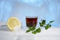 Glass cup of strong black tea on a beautiful blue ice with yellow lemon and green mint. Royalty Free Stock Photo