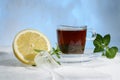 Glass cup of strong black tea on a beautiful blue ice with yellow lemon and green mint. Royalty Free Stock Photo