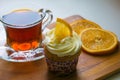 A glass cup of tea, a cupcake with orange slices on a wooden tray. Royalty Free Stock Photo