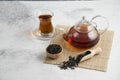 A glass cup of tea with dried loose teas and teapot