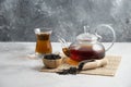 A glass cup of tea with dried loose teas and teapot