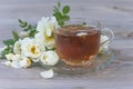 Glass cup of tea and white wild rose flowers on wooden background Royalty Free Stock Photo