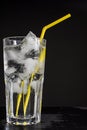 Glass cup with water, many ice cubes and yellow straw on a black background Royalty Free Stock Photo