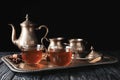 Glass cups with hot tea on tray against dark background