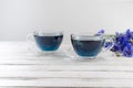glass cups and teapot of Butterfly pea tea. Anchan clitoria ternatea on a white wood background. with bouquet of blue flowers