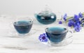 glass cups and teapot of Butterfly pea tea. Anchan on a white marble background. with bouquet of blue flowers