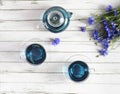 glass cups and teapot of Butterfly pea tea. Anchan on a white wood background. with bouquet of blue flowers