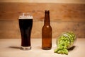 A glass of dark beer with a bottle and hop