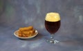 Glass of dark beer with foam and a plate with wheat croutons on a gray abstract background