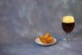 Glass of dark beer with white foam and a plate with fresh wheat croutons on a gray background Royalty Free Stock Photo