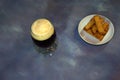 A glass of dark beer with white foam and a plate of fresh wheat croutons are nearby Royalty Free Stock Photo