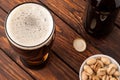 glass of dark cold frothy beer, nuts, bottle, cap, old wooden ta Royalty Free Stock Photo