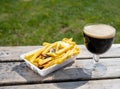 Glass of dark strong belgian beer and portion of fried potato chips with sauce and onion, served on outdoor terrace with green Royalty Free Stock Photo