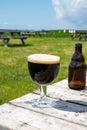 Glass of dark strong belgian beer served on outdoor terrace with green grass meadow on background Royalty Free Stock Photo