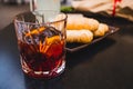 Glass of dark vermouth drink with slice of orange on a bar table outdoors, a popular aperitif, during a summer day with snacks and Royalty Free Stock Photo