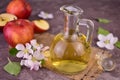 Glass decanter with apple cider vinegar and fresh apples on gray background.