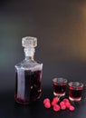 A glass decanter and two glasses of homemade raspberry liqueur on a black background Royalty Free Stock Photo