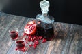 A glass decanter and two glasses of pomegranate liqueur on a wooden table, next to a ripe fruit and a handful of seed Royalty Free Stock Photo