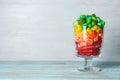 Glass of delicious chewing candies on wooden table against light background