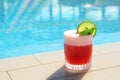 Glass of cocktail near swimming pool, space for text. Refreshing drink Royalty Free Stock Photo