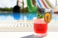 Glass of cocktail near swimming pool, space for text. Refreshing drink Royalty Free Stock Photo