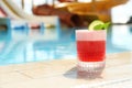 Glass of cocktail near swimming pool, space for text. Refreshing drink Royalty Free Stock Photo