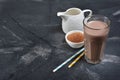 Glass of delicious cold chocolate milk drink with white jug and cocoa powder