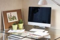 Glass desk with computer, succulents in green pots, lamp, watercolor picture, watercolor paints and cork board.