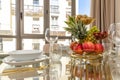 A glass dining table with a gold fruit bowl with pineapple, various types of grapes, kiwi, red apples, gold cutlery