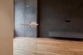 Glass door with metallic handle open in to the empty room with black wall and wooden floor.