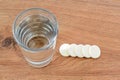 Glass of drinking water and some soluble effervescent vitamin pills on a wood background. Vitamins and nutritional supplements.