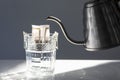 Glass with drip coffee bag and metal kettle on light grey table, closeup Royalty Free Stock Photo