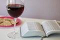 A glass of dry red wine and broken unleavened bread lie on a plate. To celebrate the Lord`s Supper. Nearby lies the Bible