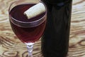 A glass of dry red wine on a wooden table with a cork floating in the glass there is a bottle of wine nearby Royalty Free Stock Photo