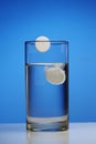 A glass with effervescent tablets on a blue background.