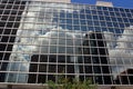 Glass facade of a modern office building with reflections of the cloudy sky.