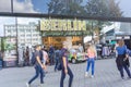 Glass facade with reflections and retail storefront with name BERLIN over entrance and brightly painted automobile from East