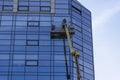 Glass faÃÂ§ade repair and maintenance at high altitude. A worker stands in a lift at a high height and repairs the glass facade of