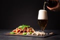 A glass filling with beer, pistachios and prosciutto seasoned with black pepper and basil on a dark background. Royalty Free Stock Photo