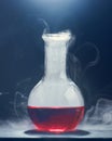 Glass flask with a red liquid smokes on a gray background. Royalty Free Stock Photo