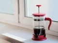 Glass Frenchpress on the windowsill in the rays of bright sunlight. The process of brewing ground black coffee. A fragrant drink